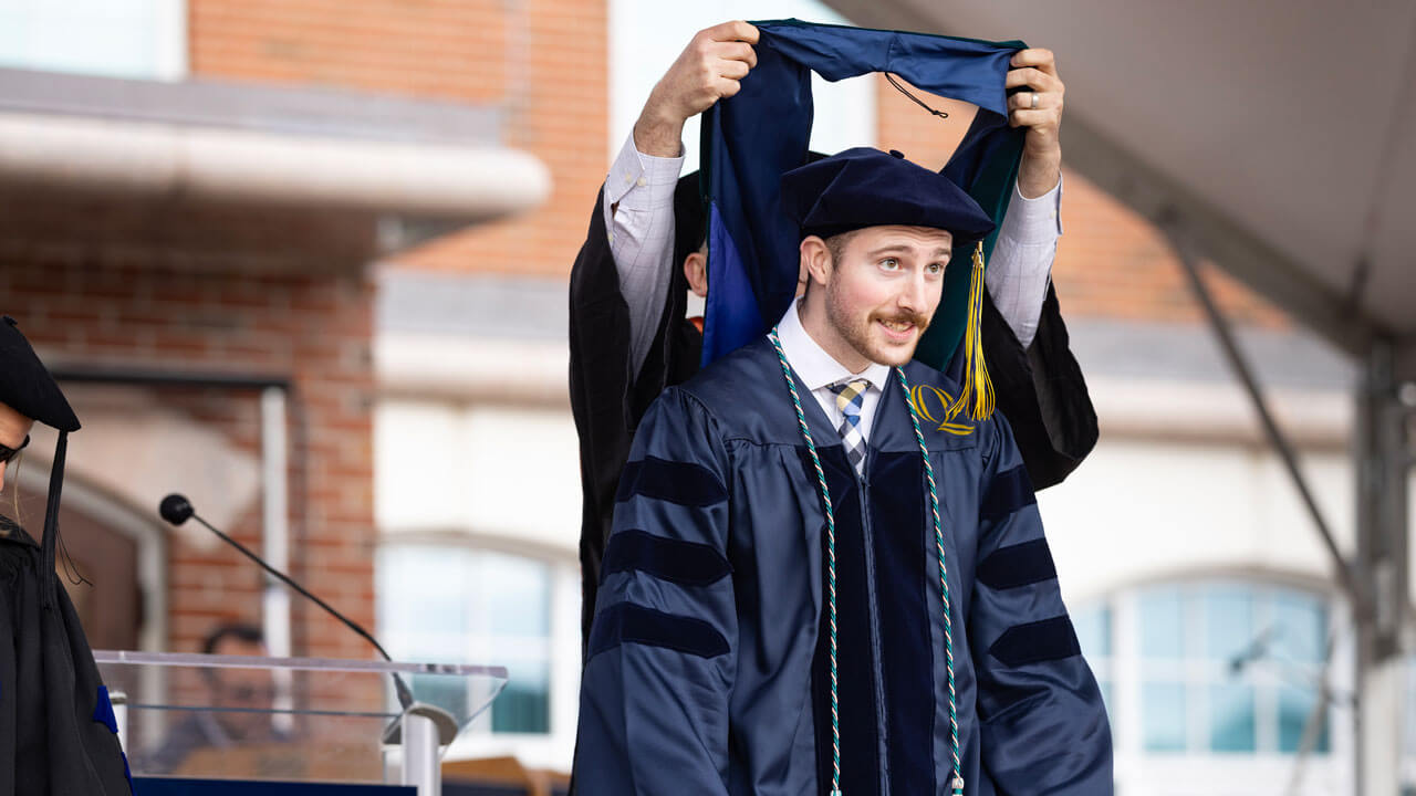 After crossing the stage, a class of 2024 Health Sciences graduate is awarded a green hood.