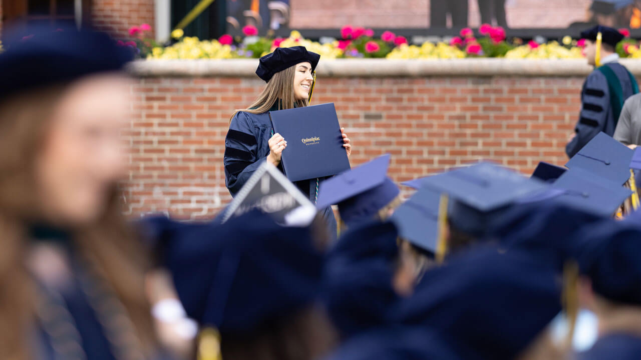 A happy graduate student holds their diploma out in front of them proudly.