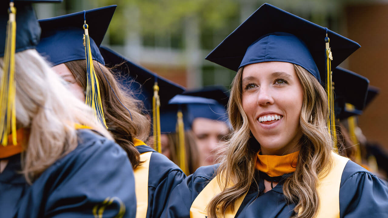 A proud health science graduate smiles broadly while sitting with their peers during the Commencement ceremony.