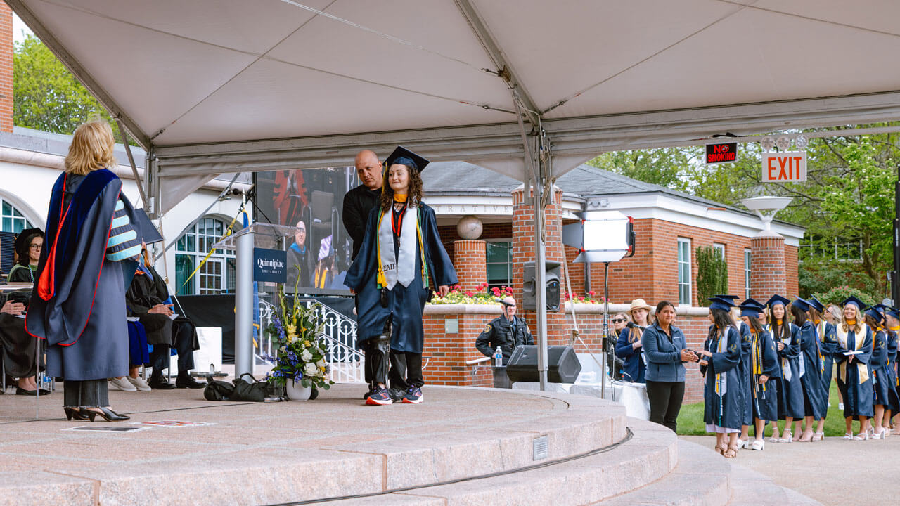 Graduate student Nicole Cyr crosses the stage to receive their diploma from President Olian.