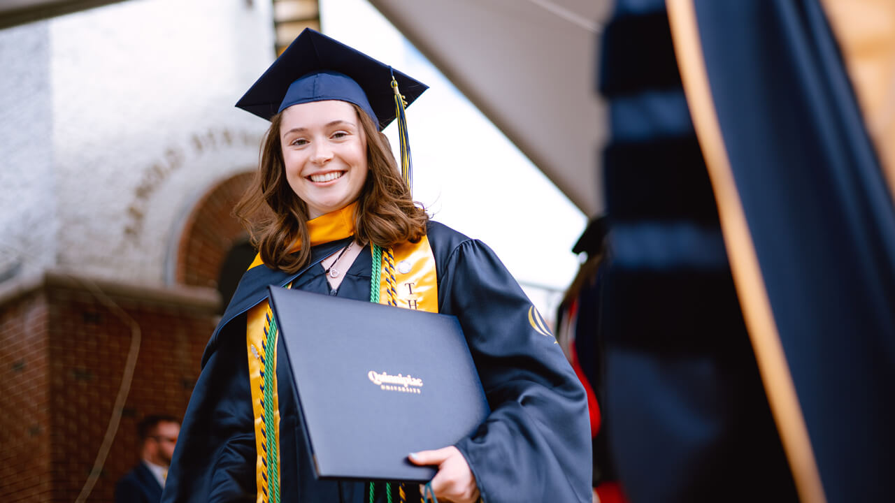 Student smiles at camera holding degree