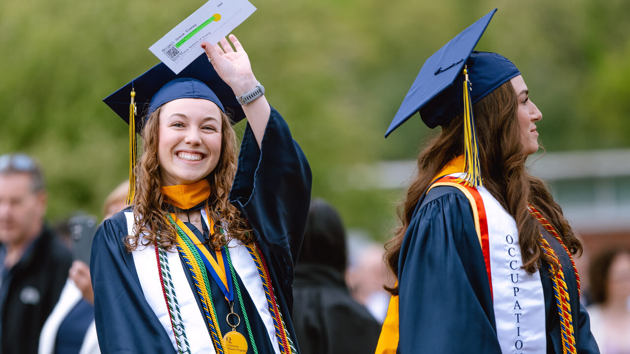 A graduate holds up her hand and waves to her family