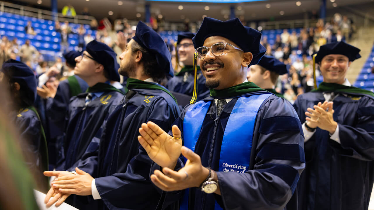 Several graduates clap as they stand