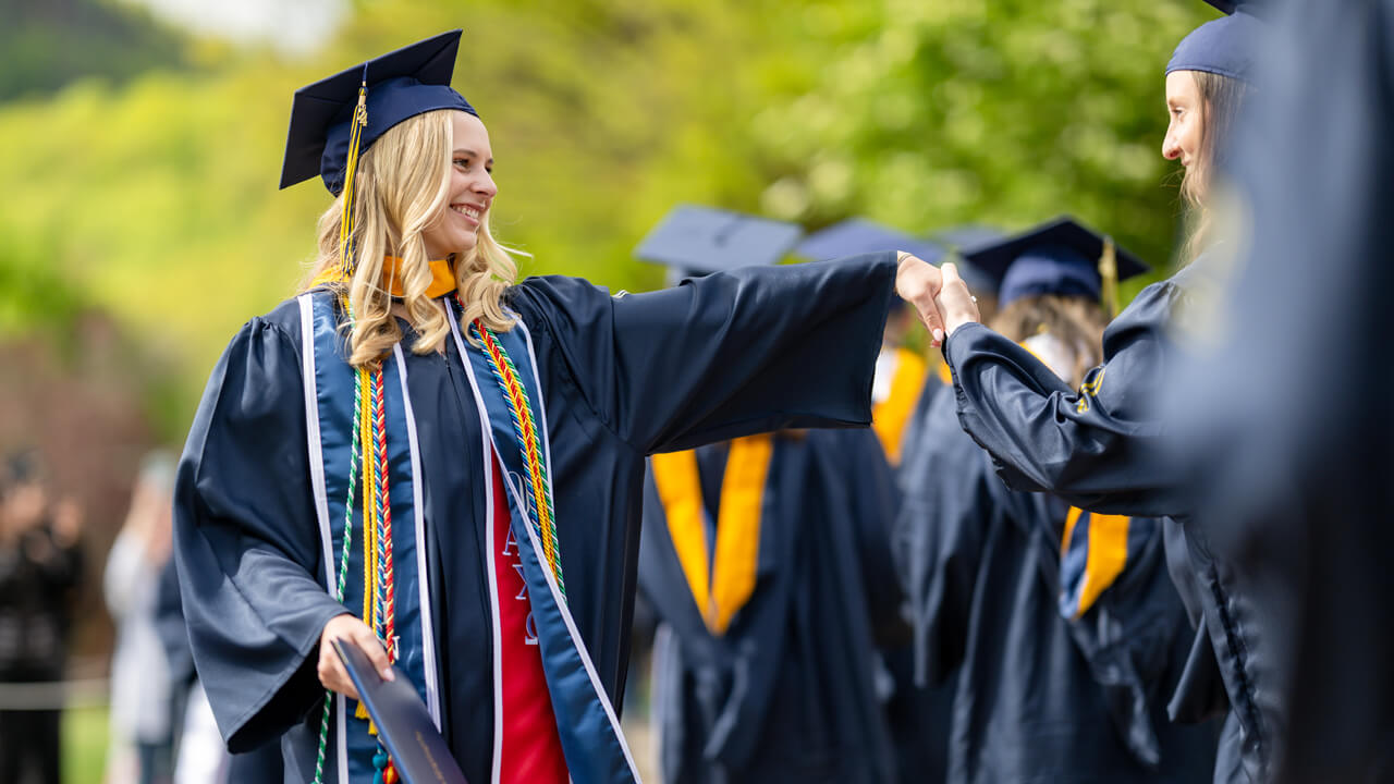 Two graduates clasp hands as they walk past each other