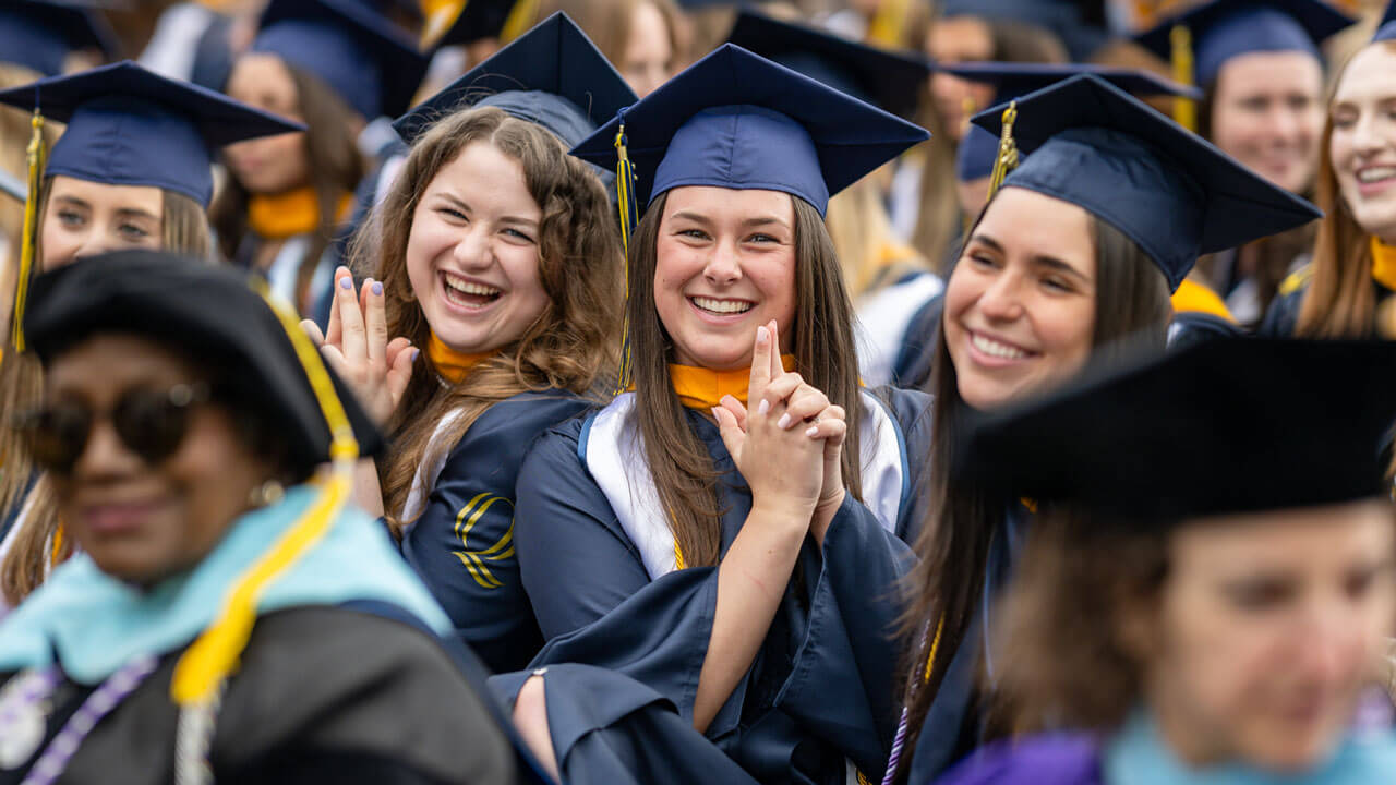 2 Class of 2024 graduates strike a pose for a photo while excitedly waiting to receive their diplomas.