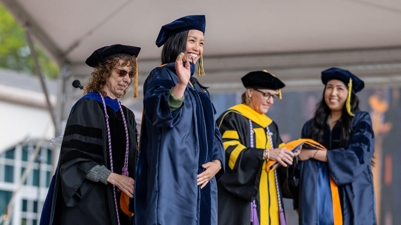 Graduate waves to the audience while standing on the library steps.