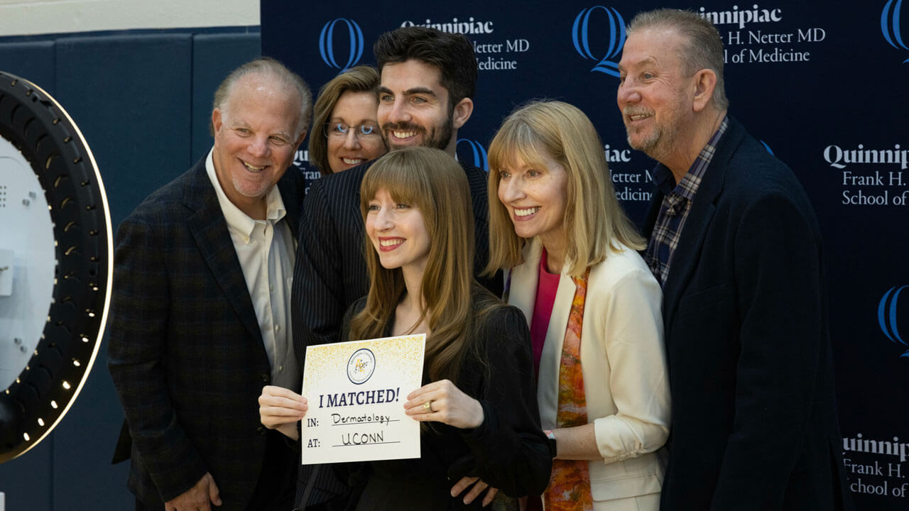 Student takes a photo with their family in front of the Quinnipiac photo booth