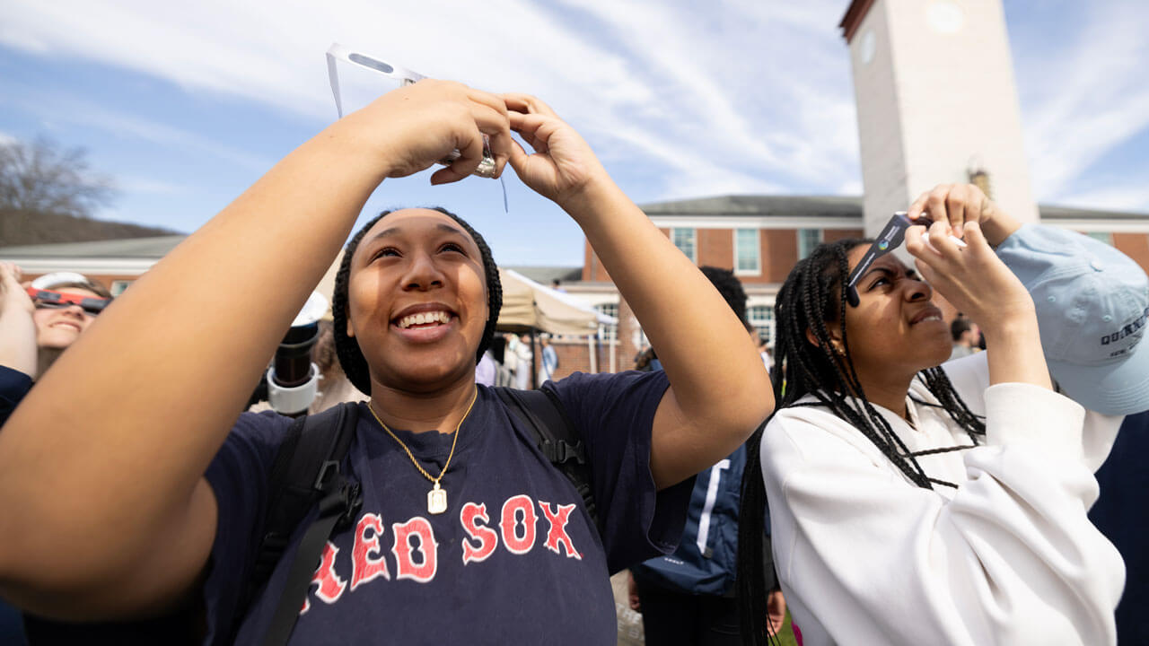 A student takes a photo with their phone through solar eclipse glasses.