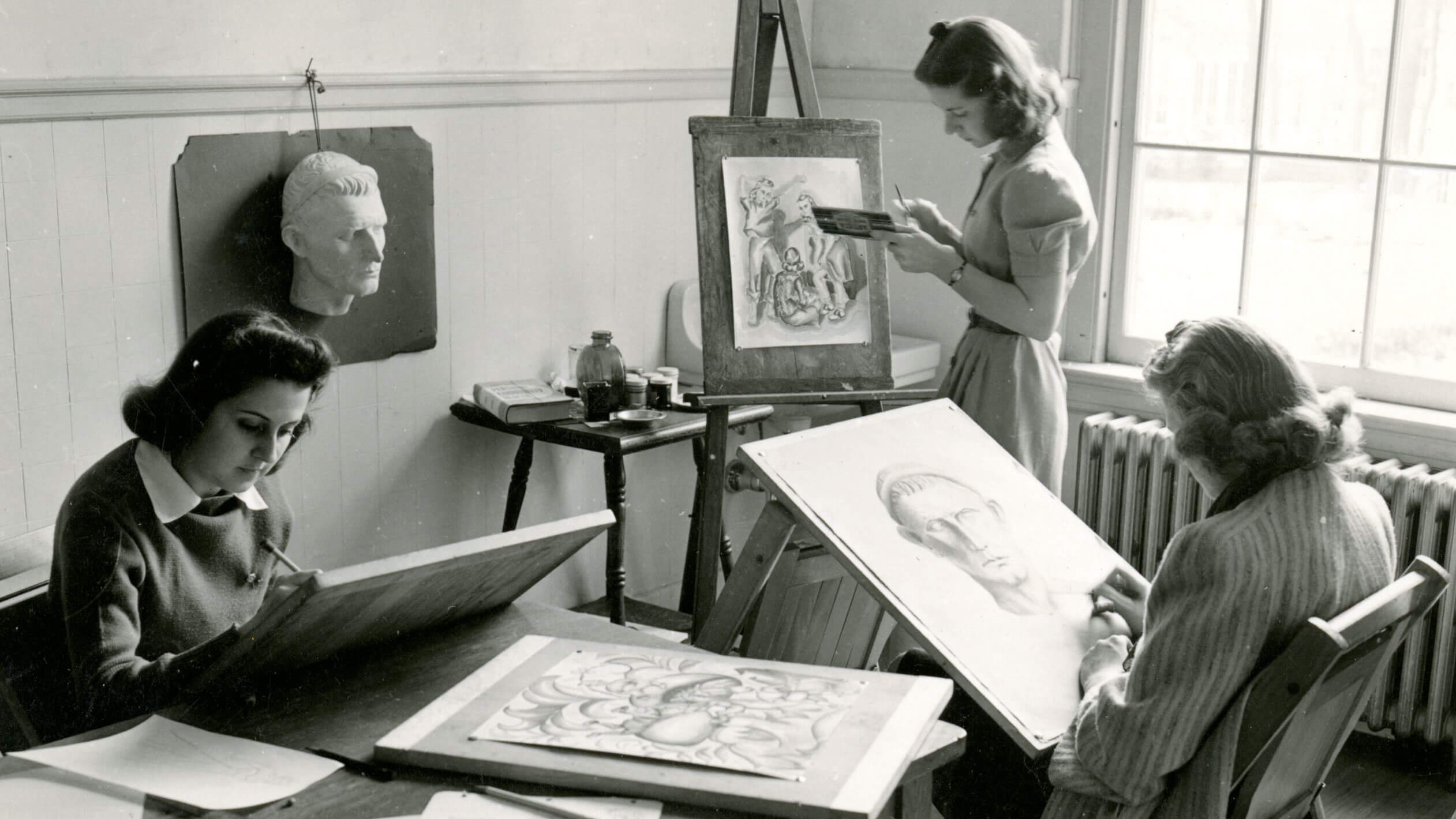 Three women drawing intricate figures on canvases