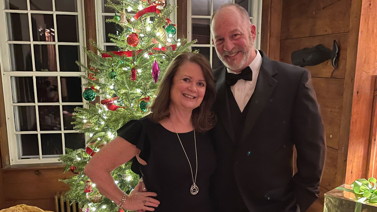 Bob Quarz and Sheila McCarthy smile in front of a Christmas tree.