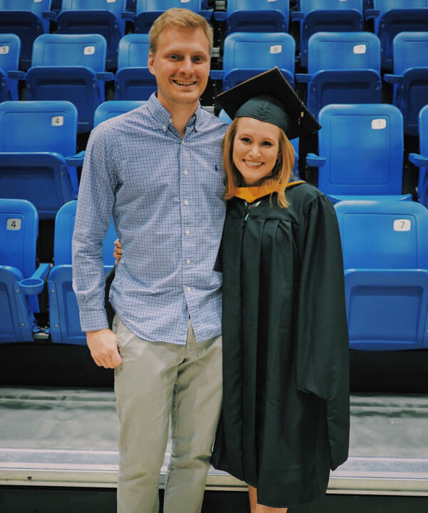 Emma wears a graduation cap and gown, standing next to Spencer.