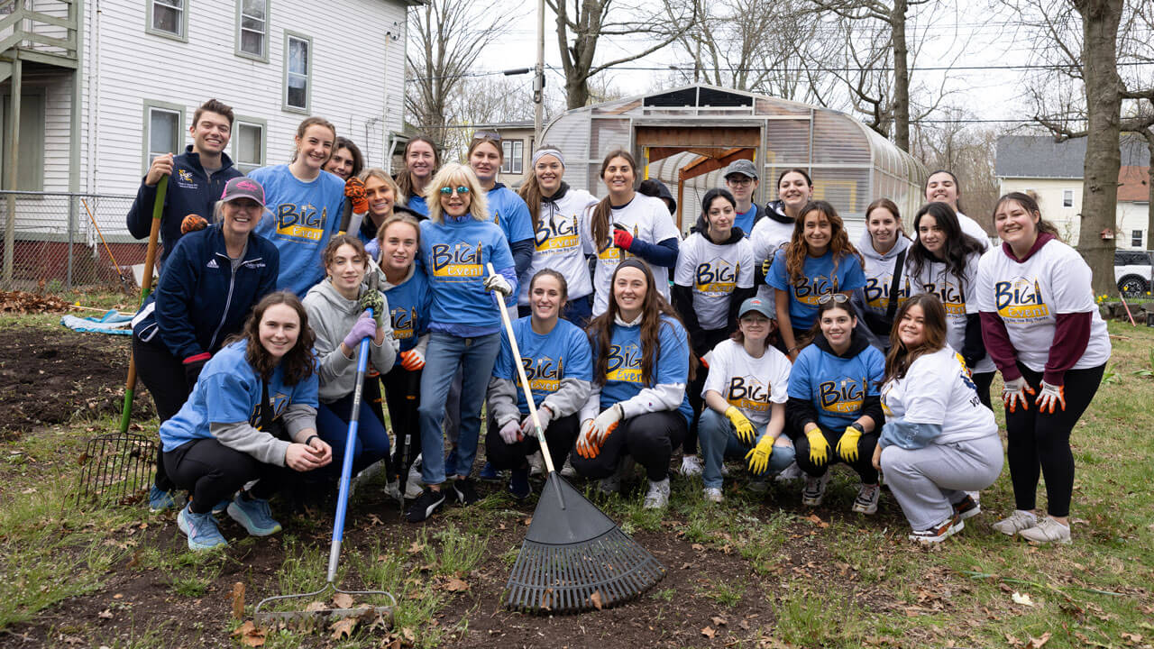 Students pose for a photo with President Judy Olian holding rakes and gardening supplies