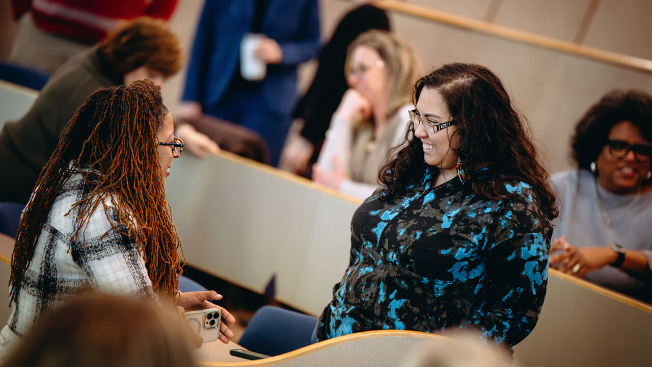 Two faculty members smile at one another.