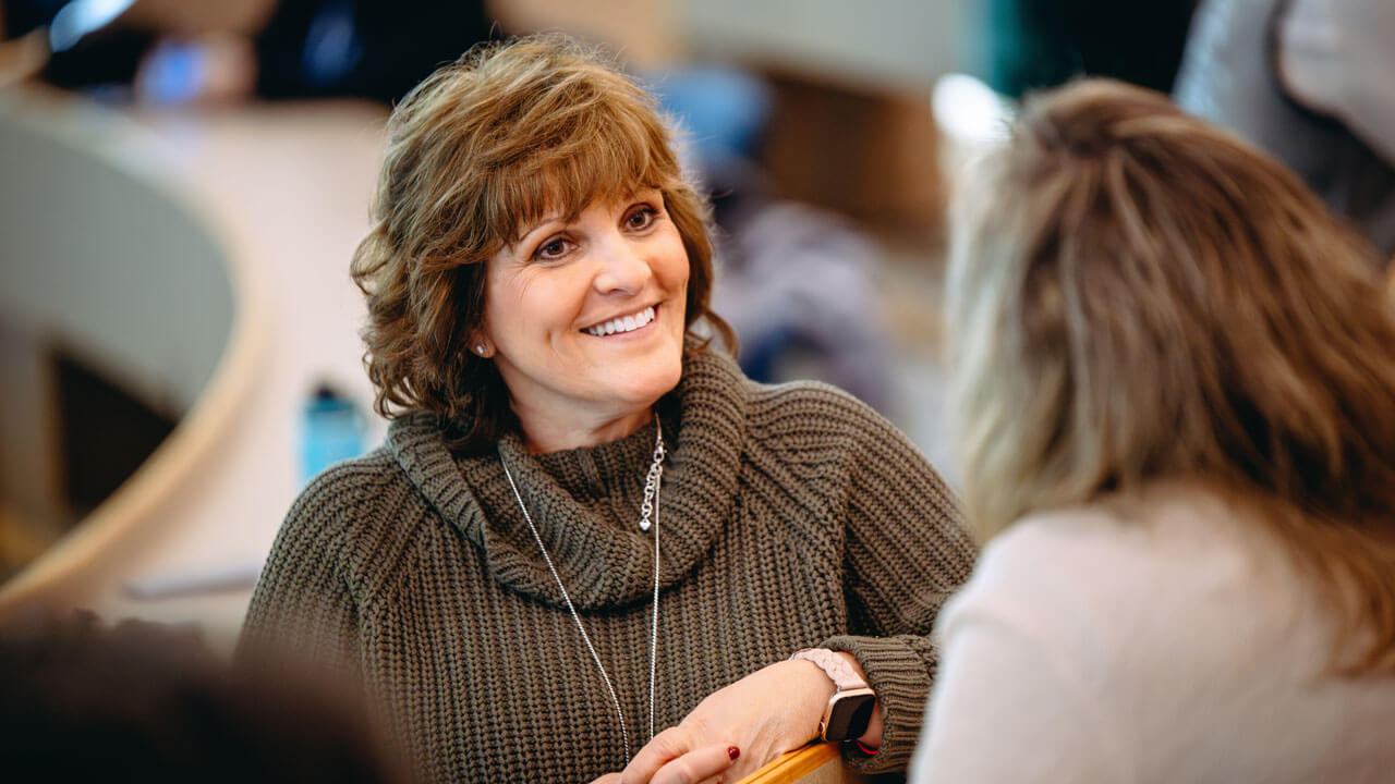 A faculty member wearing a sweater smiles at another attendee.