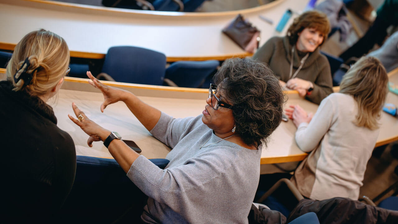 A faculty member holds out their hands, explaining something to another attendee.