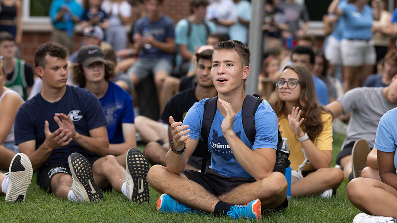 Hundreds of students sit on the quad and clap