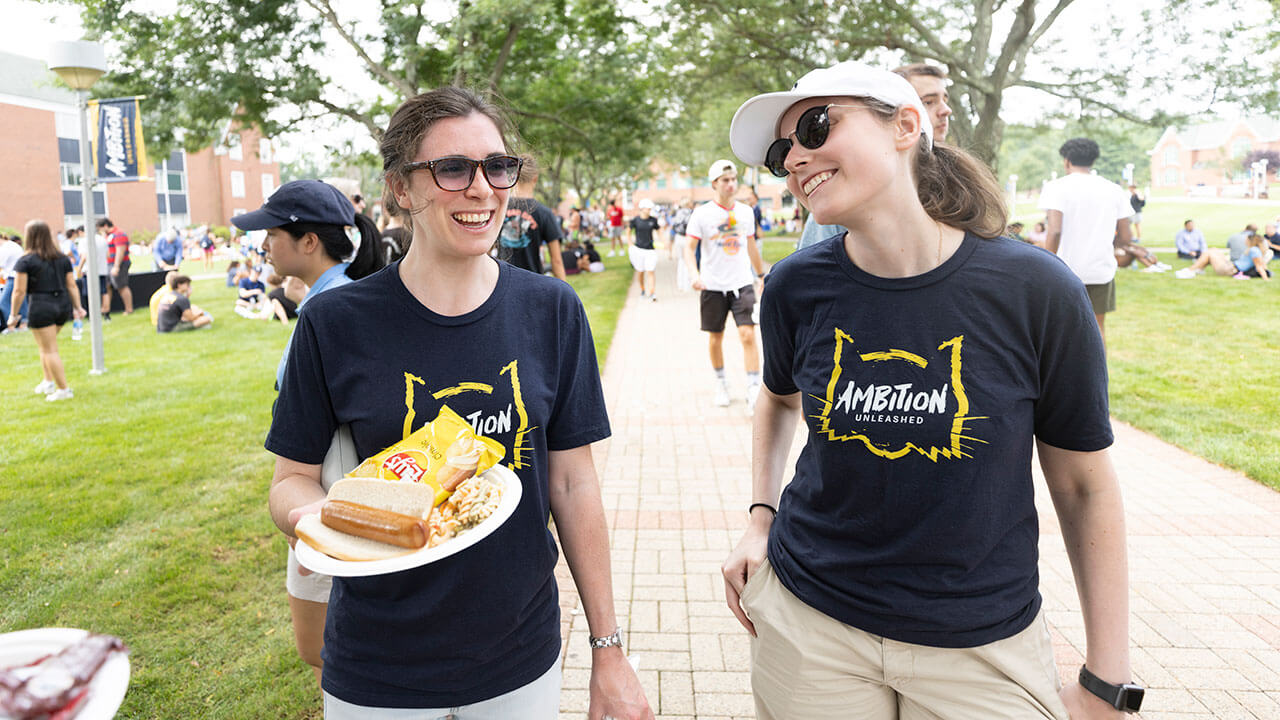 Two staff members in Ambition Unleashed tee shirts talk during the welcome barbeque