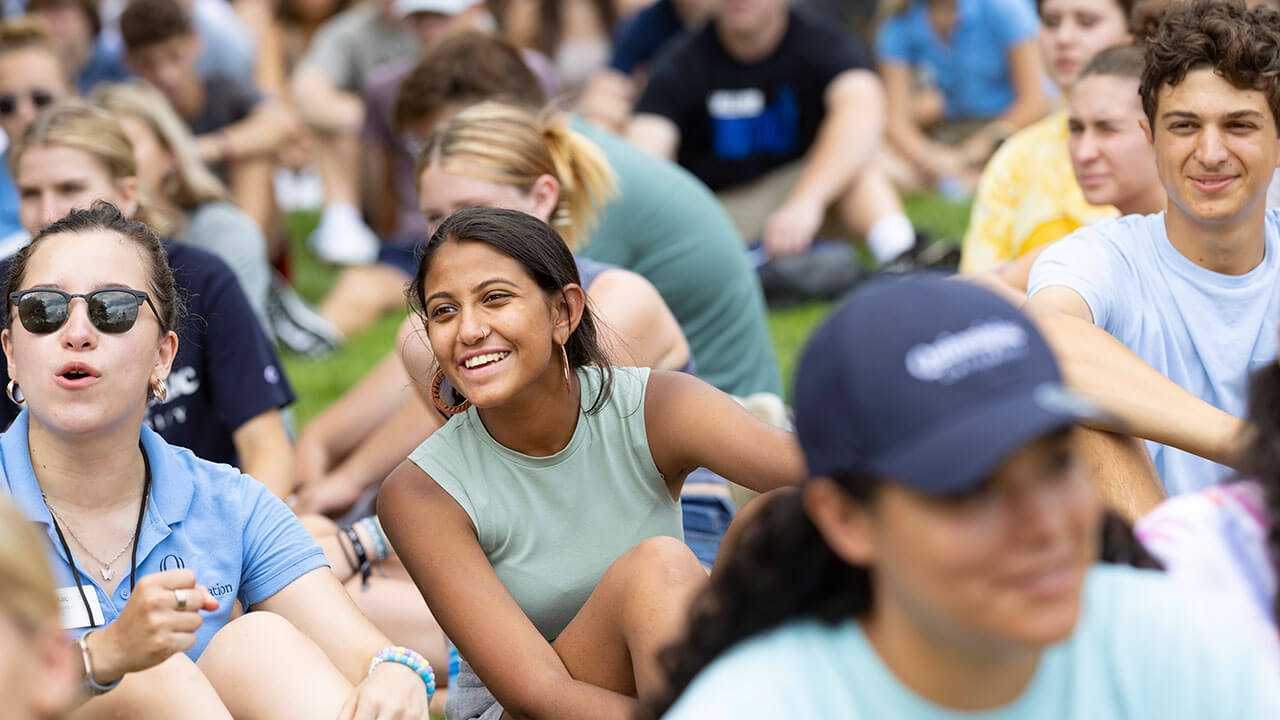 A new student and orientation leader cheer as they sit on the grass