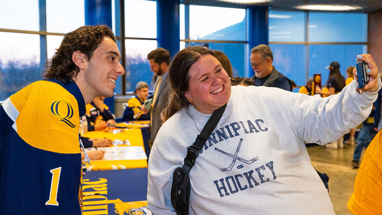 Yaniv Perets Quinnipiac mens ice hockey goaltender smiles with a fan for a selfie