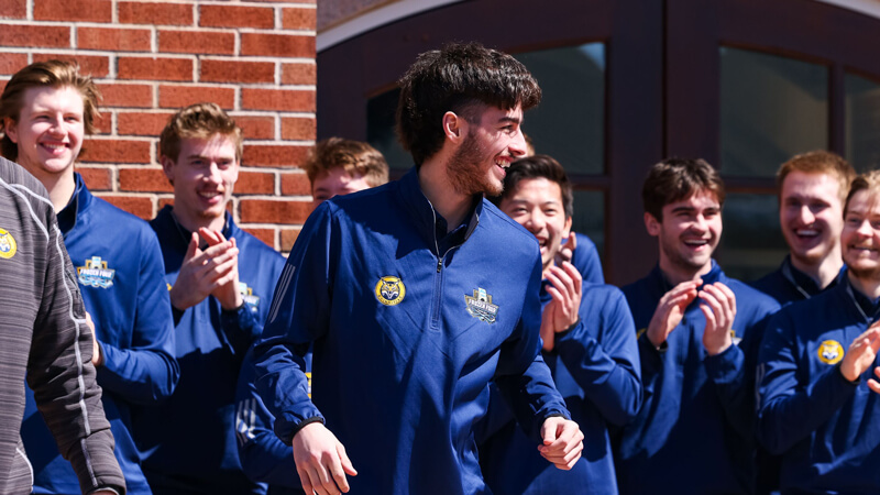 Men's ice hockey team members cheer and smile on the library steps