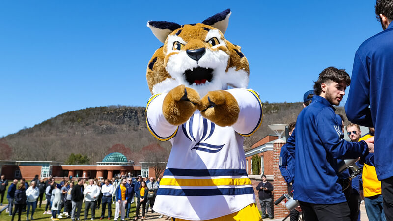 Boomer the Bobcat in his white hockey jersey points to the camera