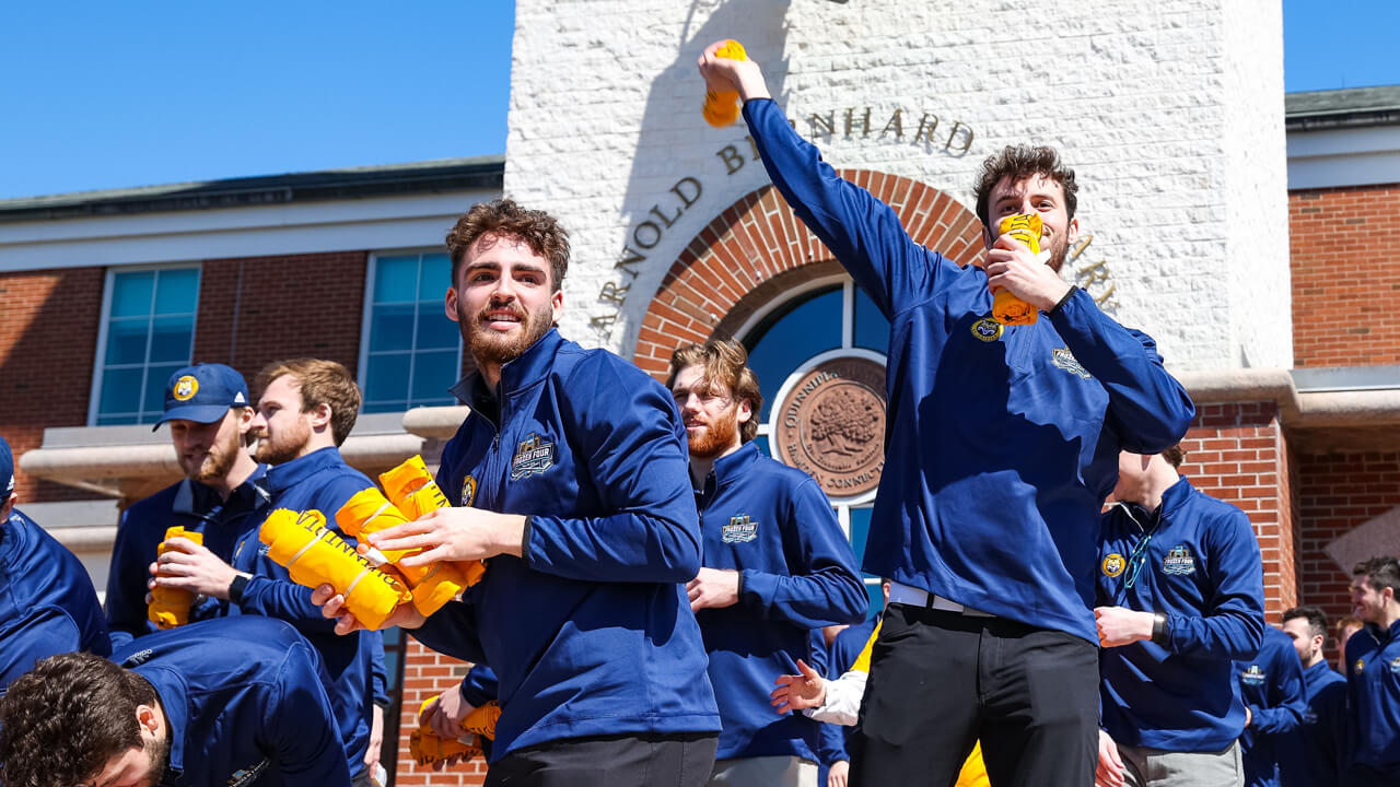 Members of the men's ice hockey team throw rolled up tee shirts from the library steps to the pep rally crowd