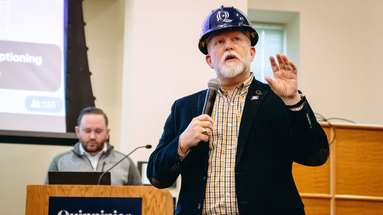 A speaker wearing a hard hat talks into a microphone.