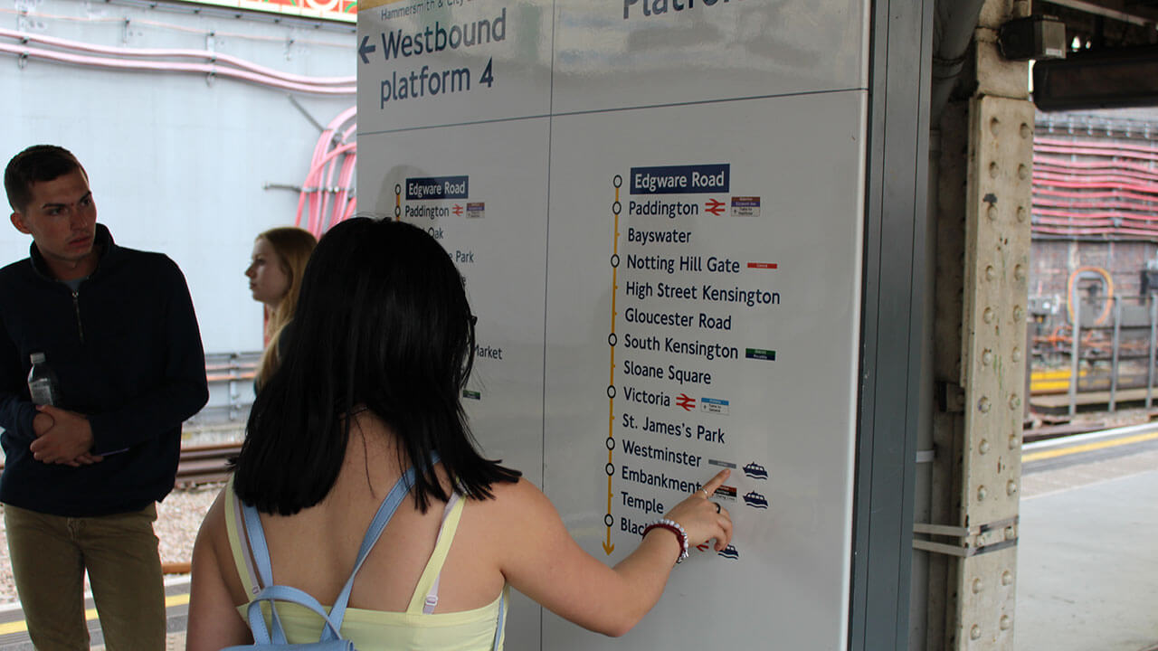 female student points at an underground subway sign, male student also looks at the sign