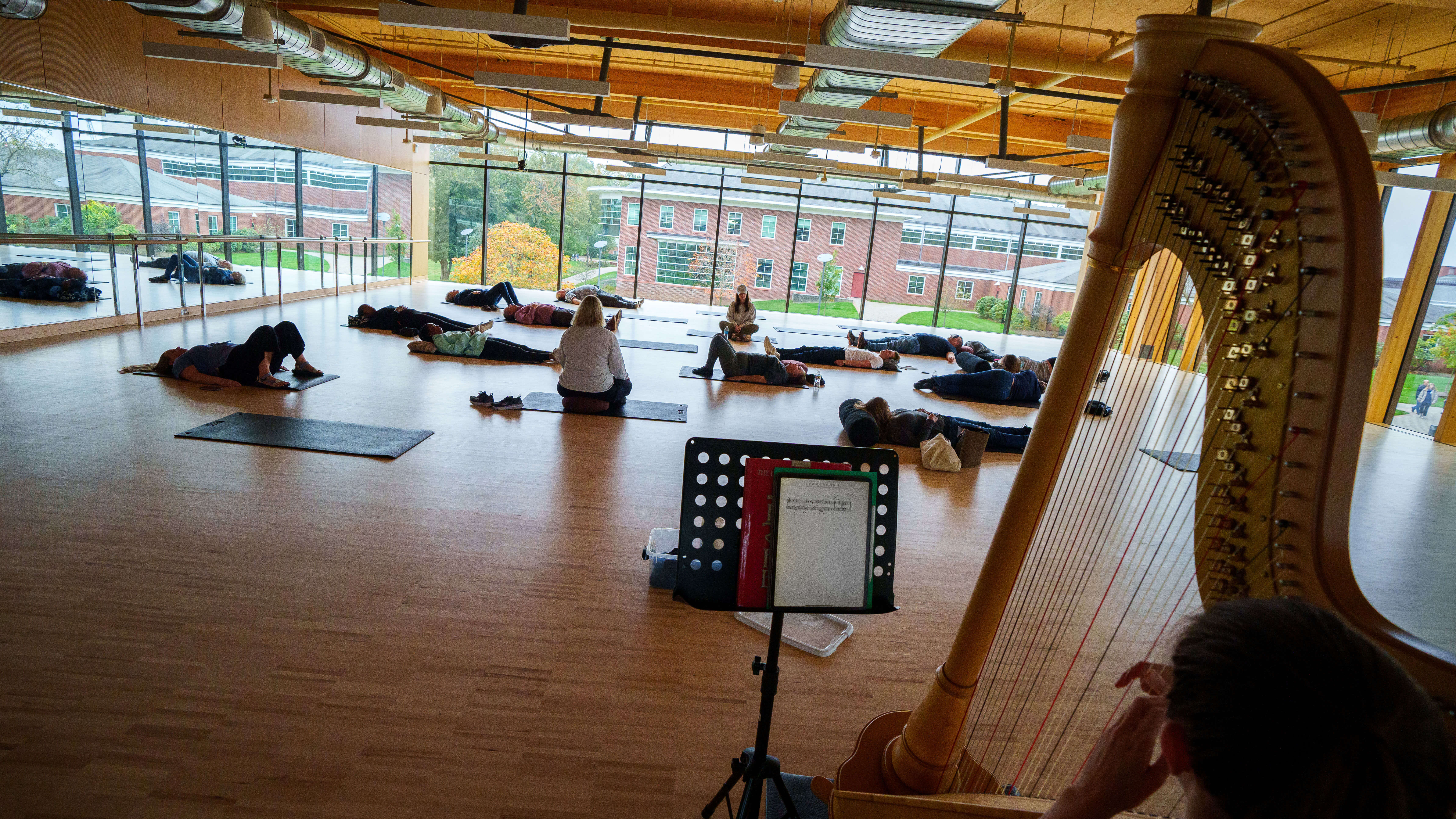 A group lays down on the floor on yoga mats while a girl plays the harp.