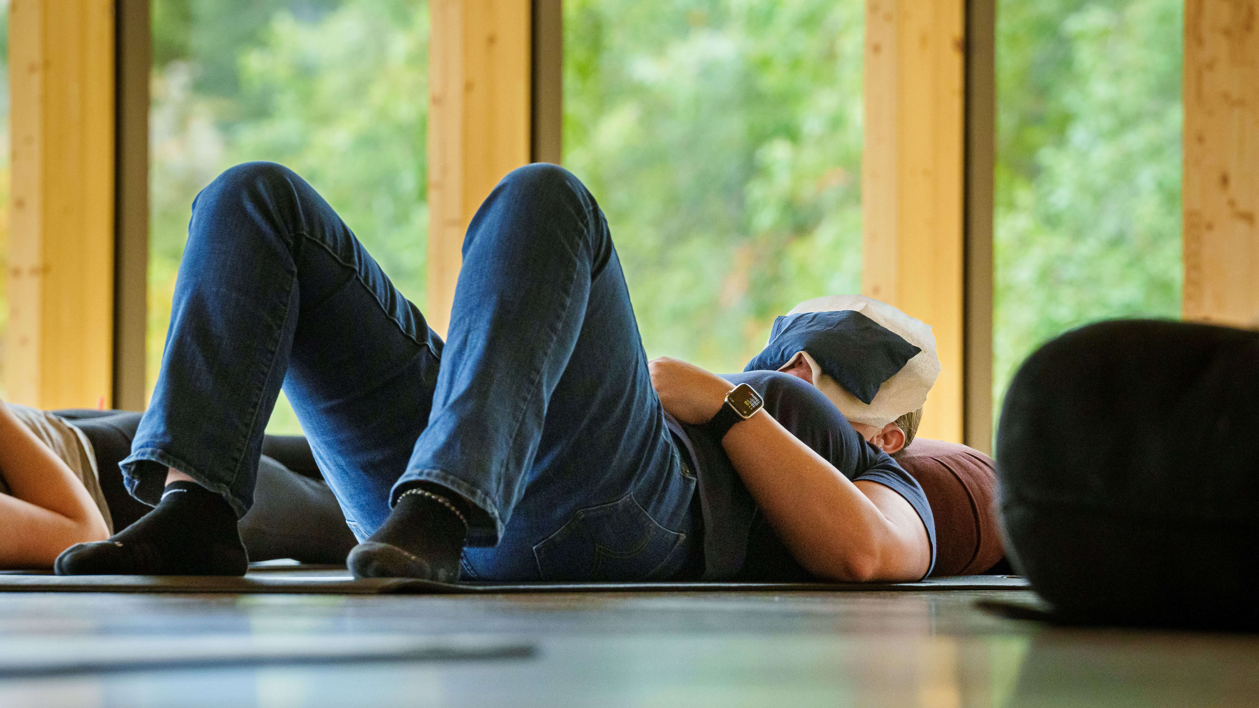 A woman lays on a yoga mat with her feet propped up and a face mask on her head.