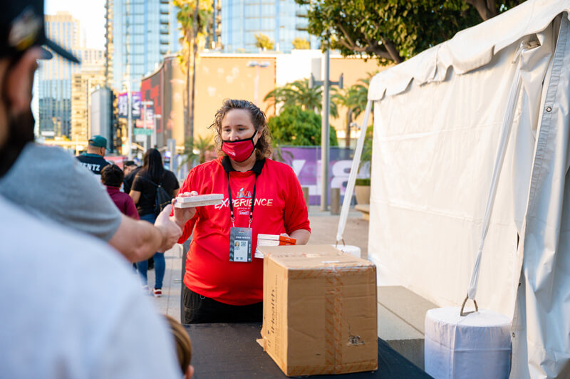 A staff member hands out rapid COVID tests near various tents