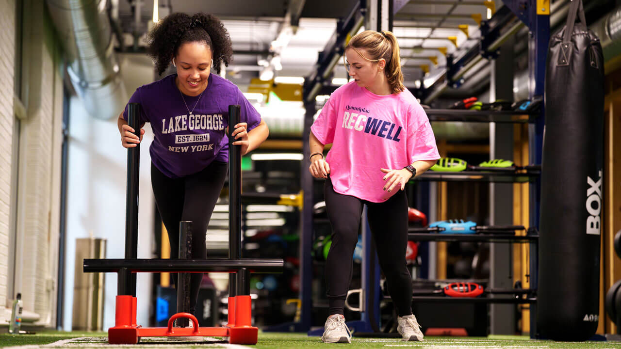 Two students help each other workout at RecWell.