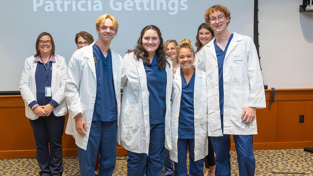 four nursing students pose smiling with their advisors wearing white coats