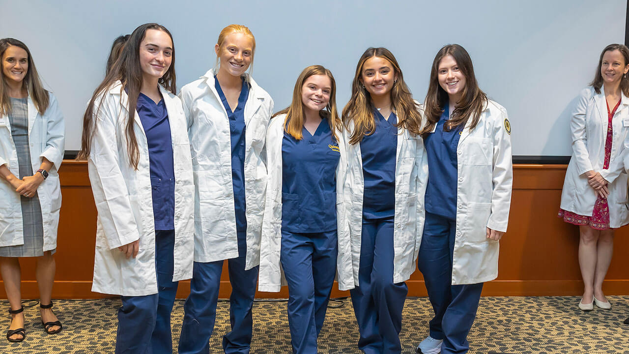 five nursing students smile together in their new white coats