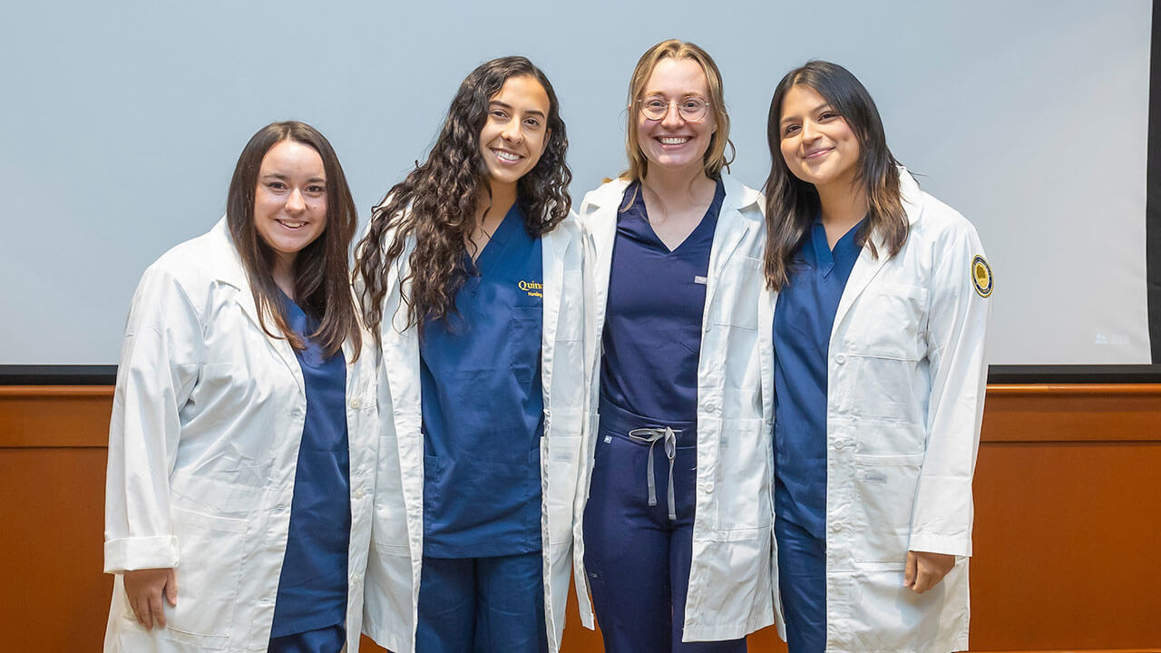 four nursing students smile for a photo while wearing their white coats