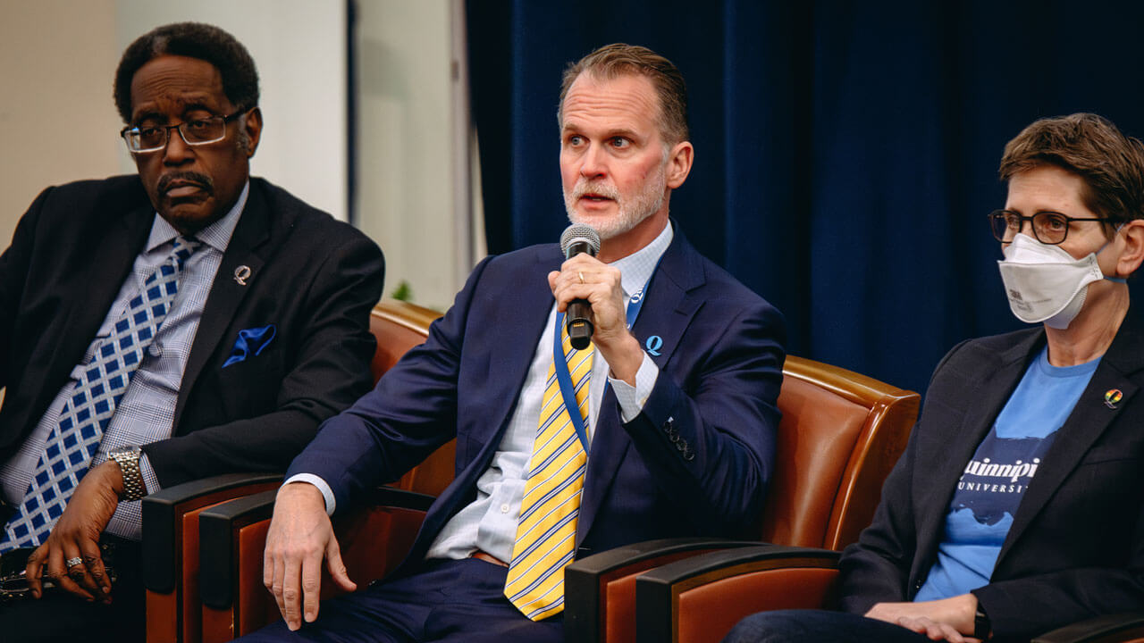 Tom Ellett talks into a microphone sitting next to senior administrators.