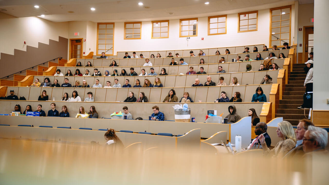 A hundred students sit and listen to speakers in the Mount Carmel Auditorium.