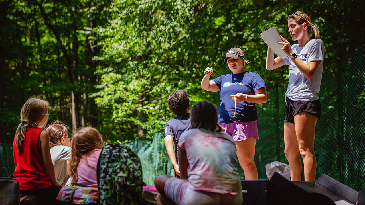 Campers sit and listen to students while they explain the field day activities