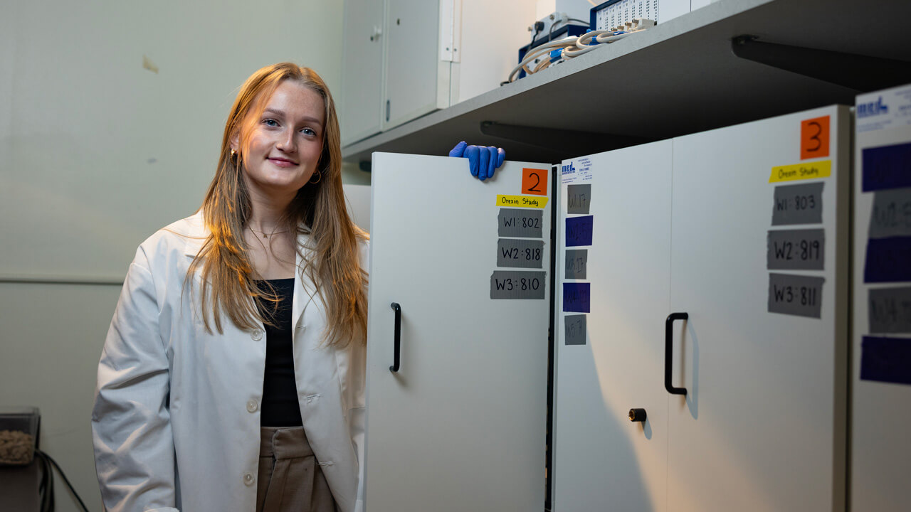 A female student opening a cabinet door smiling at the camera