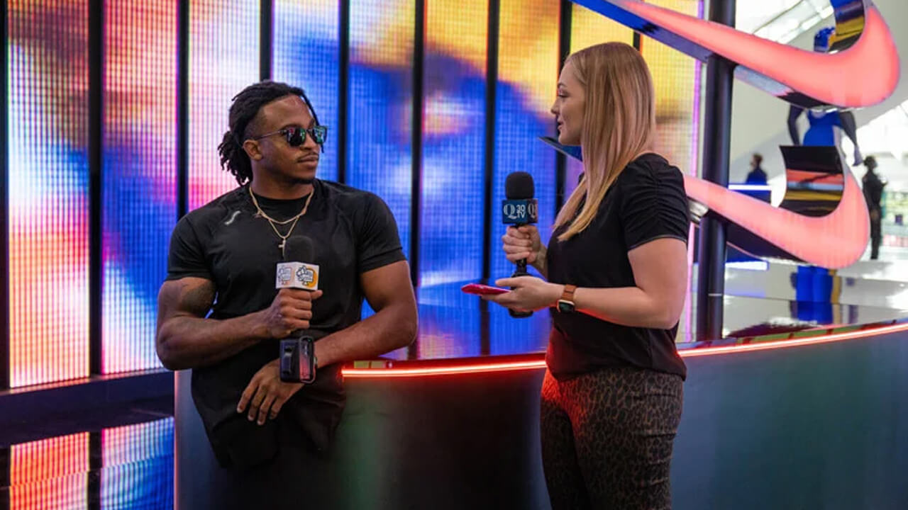 Lo Yarnall interviews Zion Clark in front of a colorfully lit wall