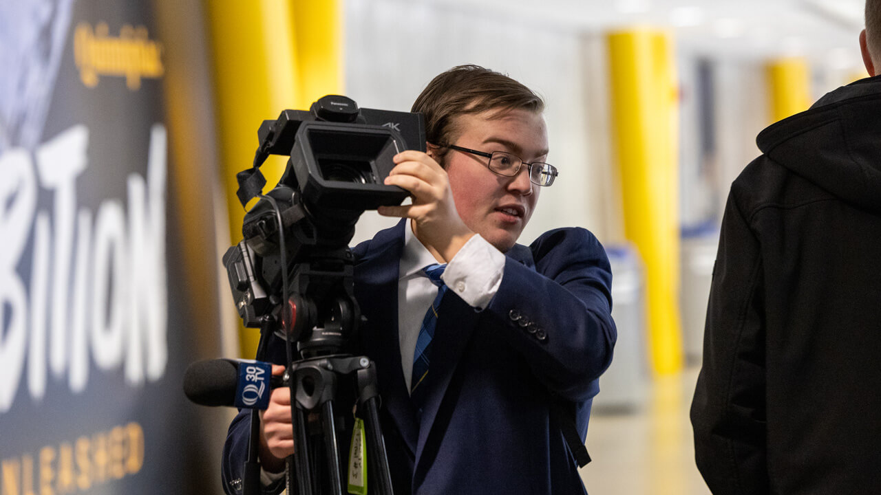 A male student carrying a camera and a Q30 microphone