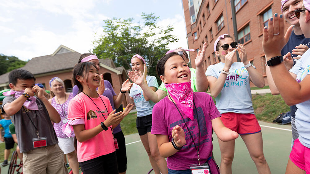 A group of children wearing pink t-shirts smile and gather around on a basketball court during a camp event