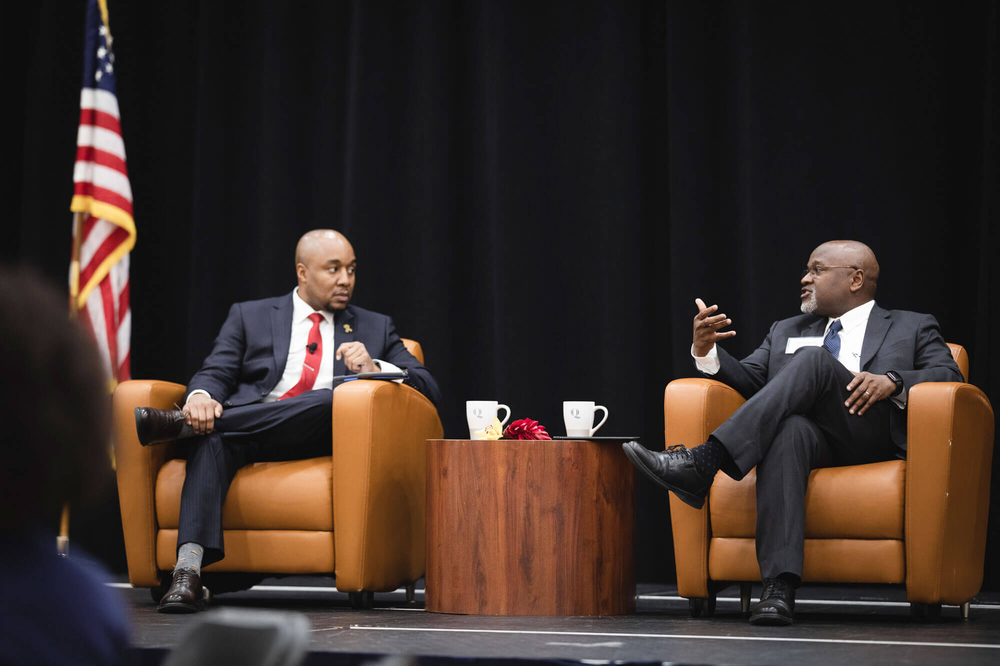 Richard Robinson and Don Sawyer talk together while sitting in armchairs on stage.