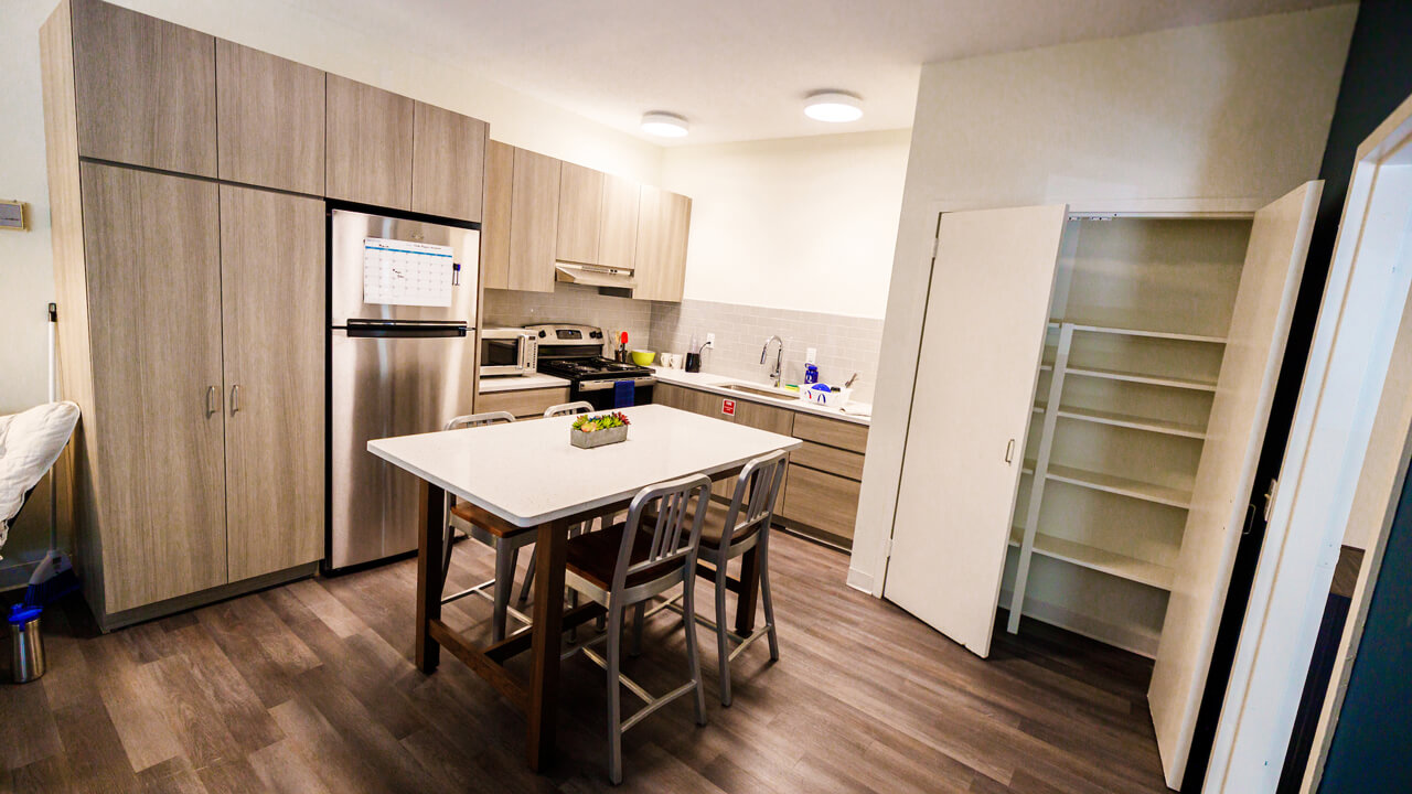 A kitchen with full fridge, microwave, stove and oven, and a full pantry, and table and chairs