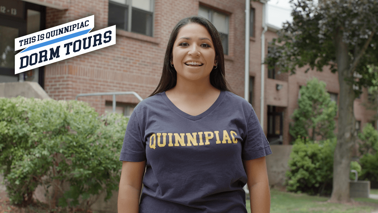 Quinnipiac dorm tours, Nicole standing in front of red brick apartment-styled housing