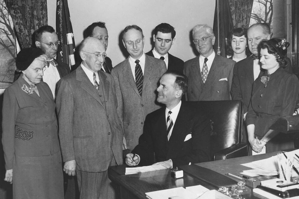 Dozens of people watch as Governor John Davis Lodge signs paperwork.