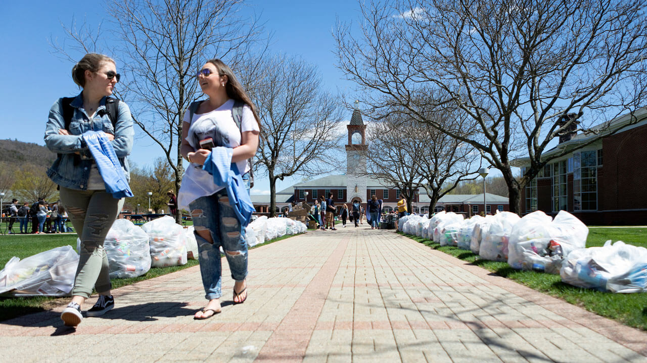 Students walking across the quad with the sidewalk lined with garbage bags