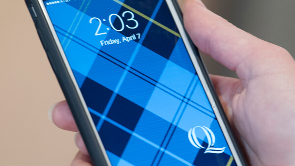 Closeup of a mobile phone with a Quinnipiac plaid background