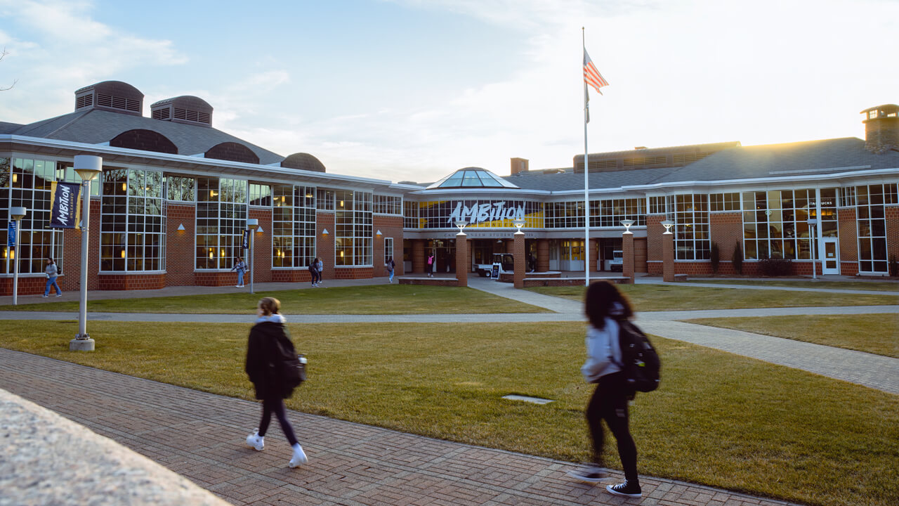 Several students walk outside the entrance of the Carl Hansen Student Center while the sun shines in the distance