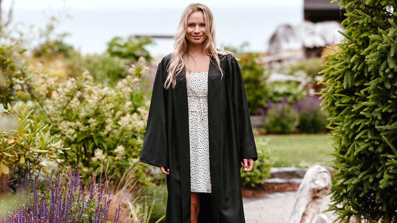 Mckenna Haz wears her commencement robe outside in a field of flowers